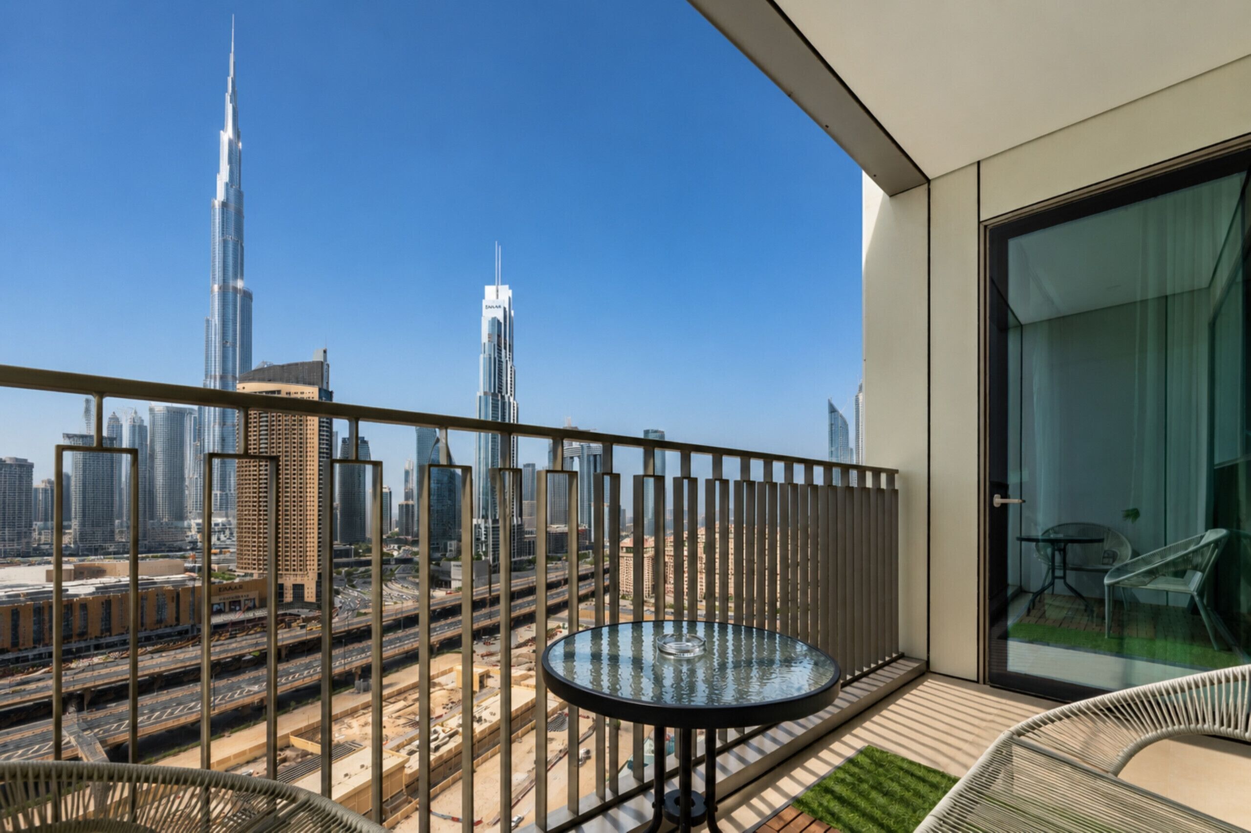 A balcony with a glass table and chairs, overlooking a cityscape with tall buildings.