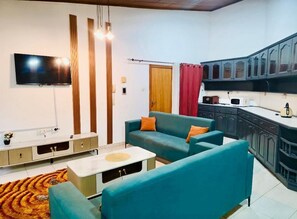 A living room with a TV, sofa, and kitchen area. - 2BR Family Apartment in East Legon (Accra)