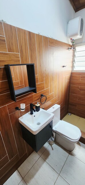 A bathroom with a wooden panel wall, a white sink, a toilet, and a towel rack. - 2BR Family Apartment in East Legon (Accra)