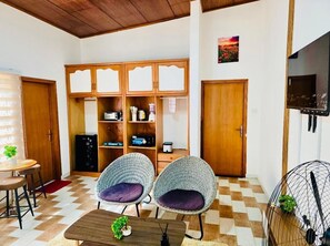 A room with two wicker chairs, a wooden cabinet, a television, and a small table with a plant. - 2BR Family Apartment in East Legon (Accra)