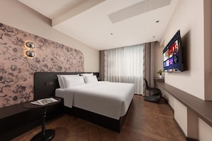 A hotel room with a large bed, a flat-screen TV mounted on the wall, a small table with a magazine, and a decorative wall with floral patterns. - Mutao Hotel Hubin in 77 (Hang Zhou Shi)