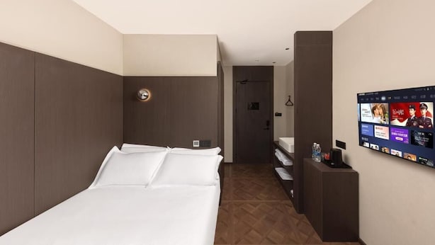 A hotel room with a bed, a TV mounted on the wall, and a wooden floor.