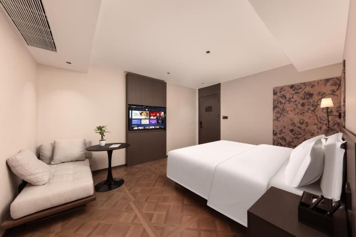 A hotel room with a bed, a sofa, a small table, a TV, and a lamp.