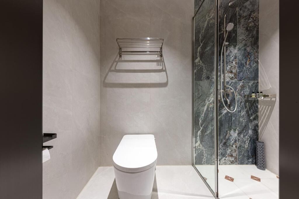 A modern bathroom with a white toilet, a glass shower enclosure, and a marble wall.