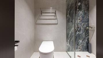 A modern bathroom with a white toilet, a glass shower enclosure, and a marble wall.