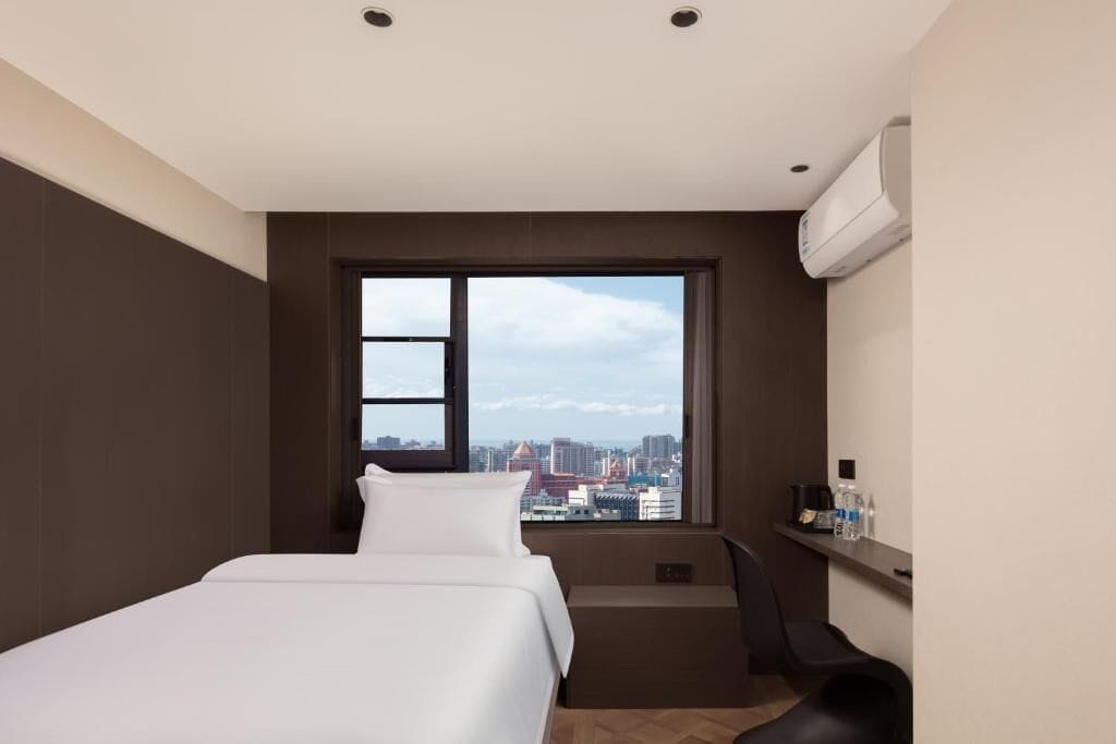 Una habitación de hotel moderna con un ventanal grande, una cama, un escritorio y una silla.