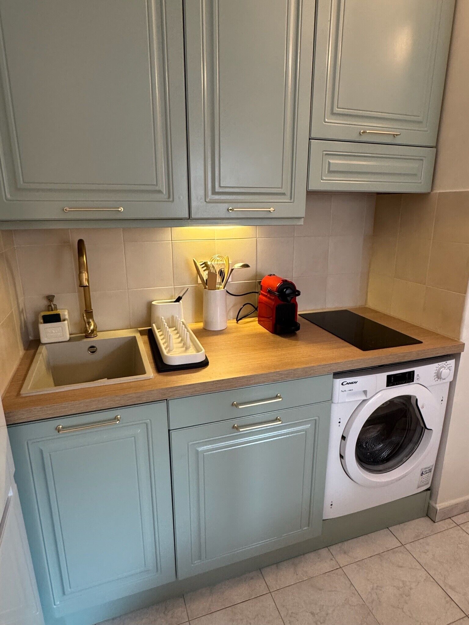 Een keuken met lichtblauwe kastjes, een spoelbak, een afdruiprek, een rode koffiezetapparaat en een wasmachine.