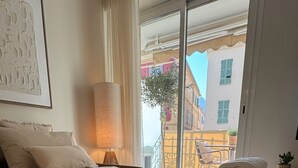 Ett hotellrum med en väl bäddad säng, en lampa, utsikt över staden och en balkong med en stol och en växt.