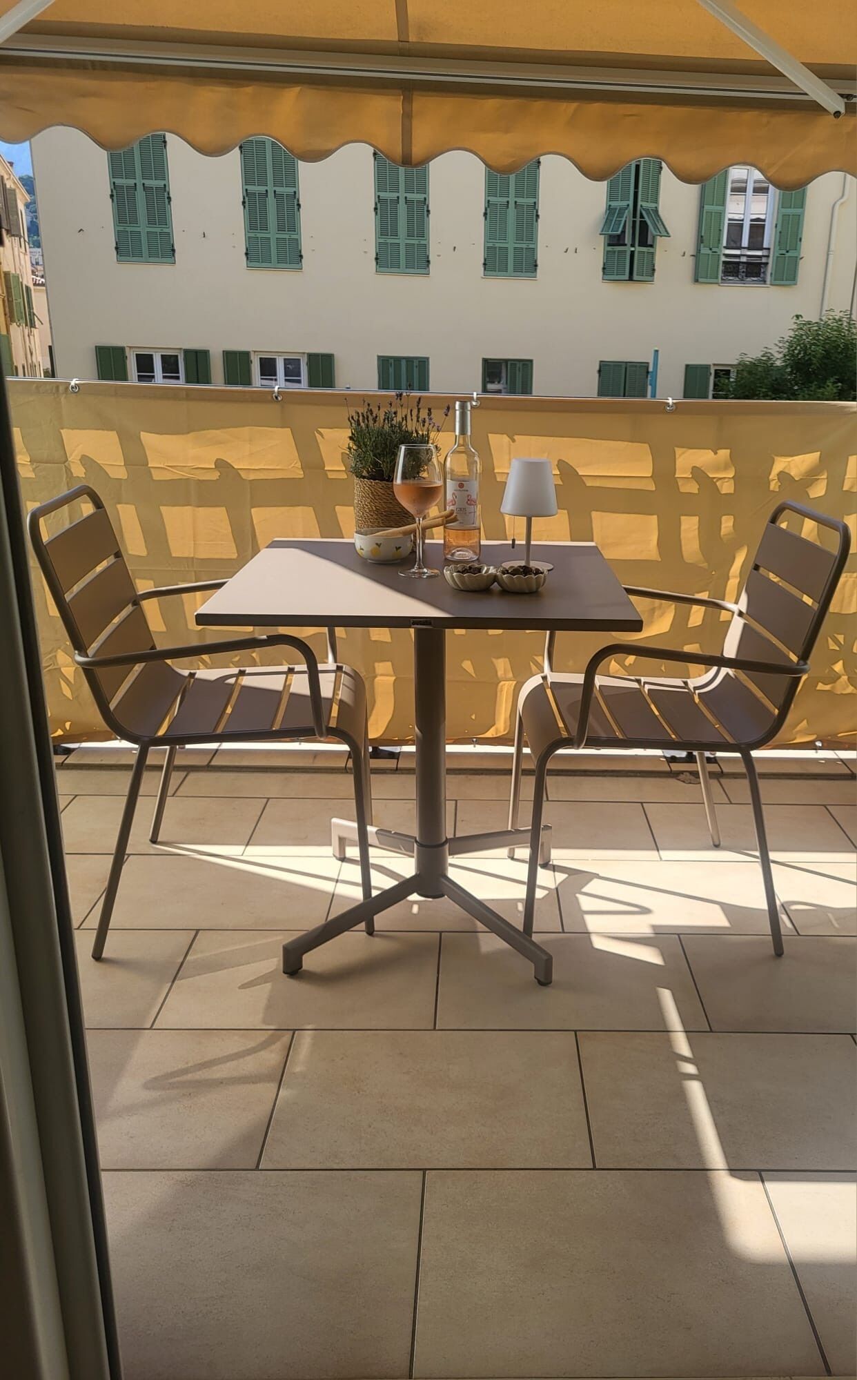 An outdoor seating area with a table and chairs, a potted plant, a bottle, and a glass.