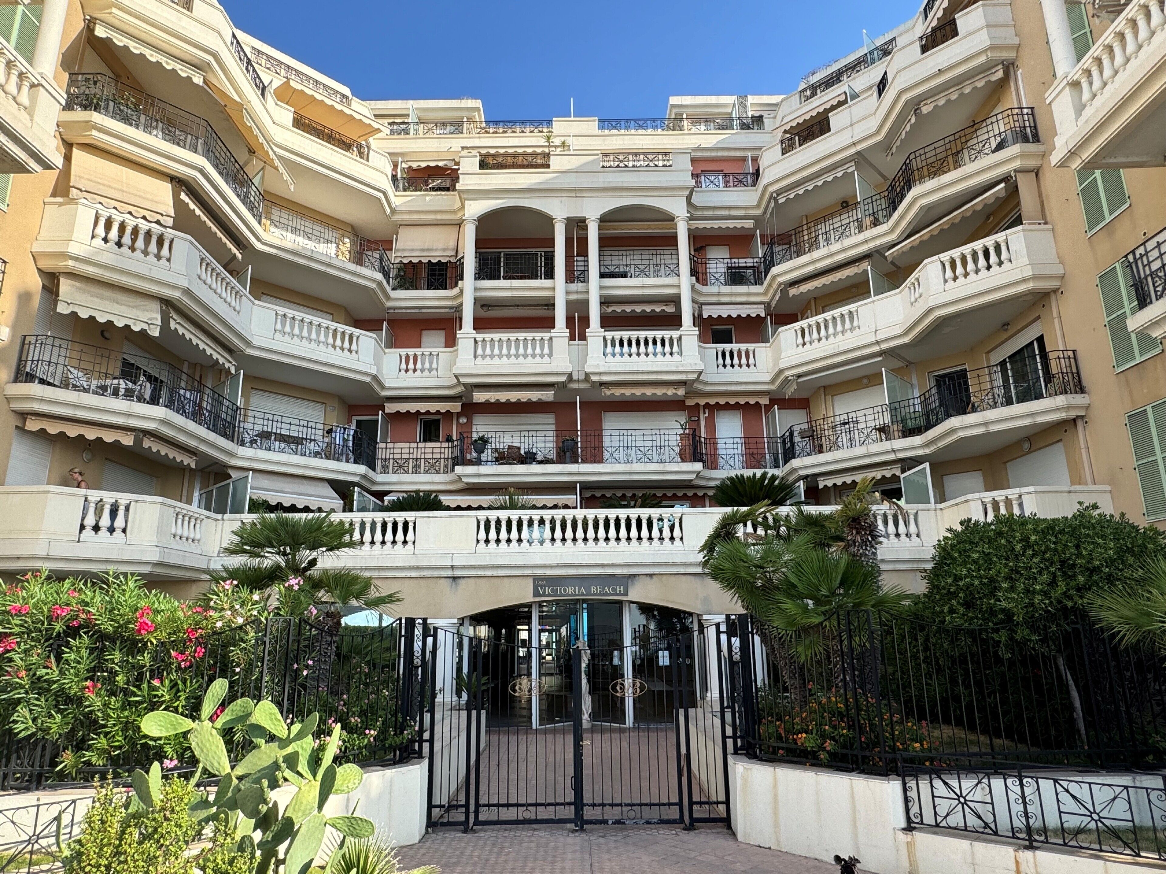 A multi-story residential building with balconies, a gated entrance, and a sign indicating 'VICTORIA BEACH'.