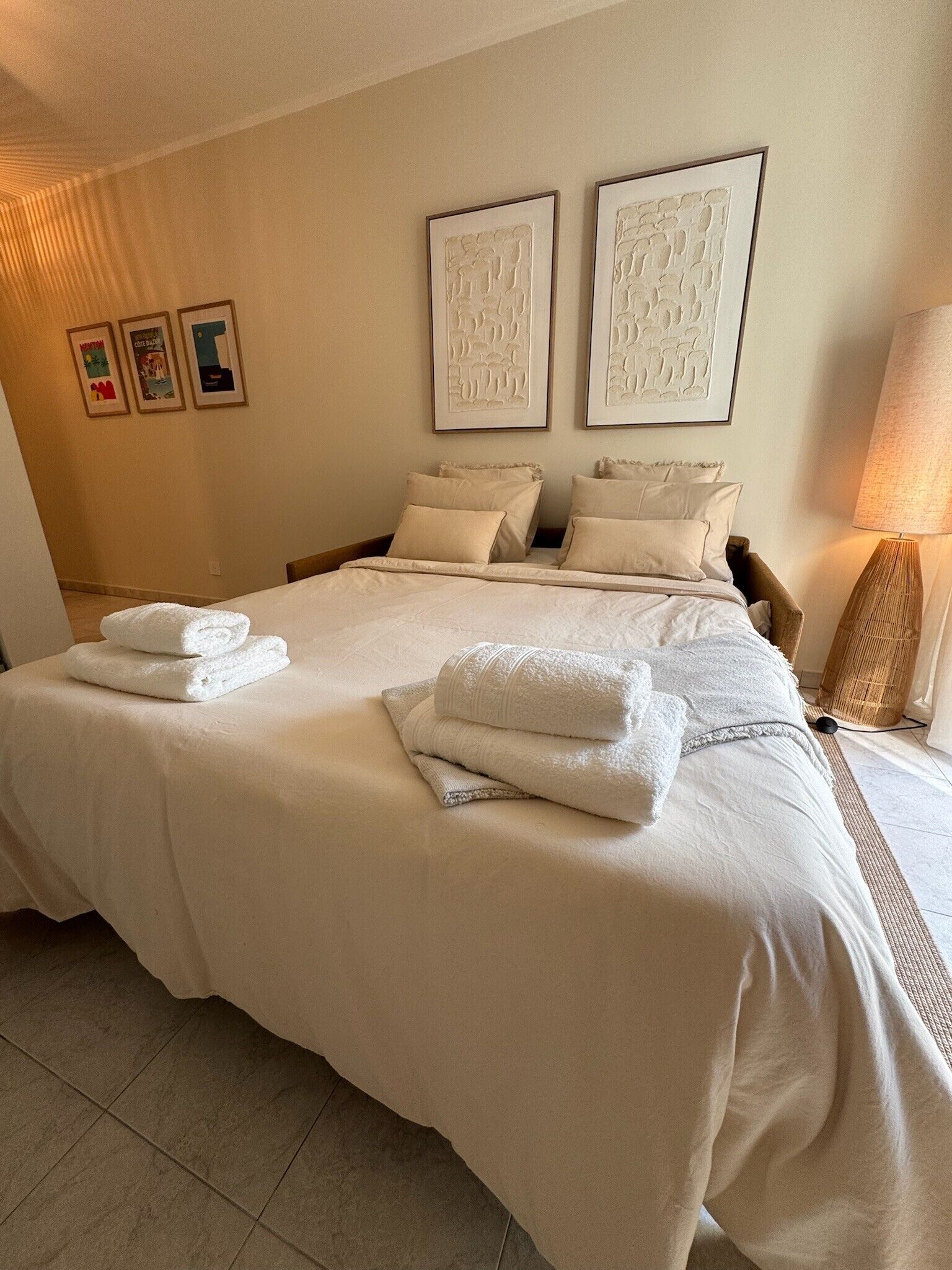 Une chambre d’hôtel avec un grand lit, deux oreillers, une lampe de chevet et trois œuvres d’art encadrées accrochées au mur.
