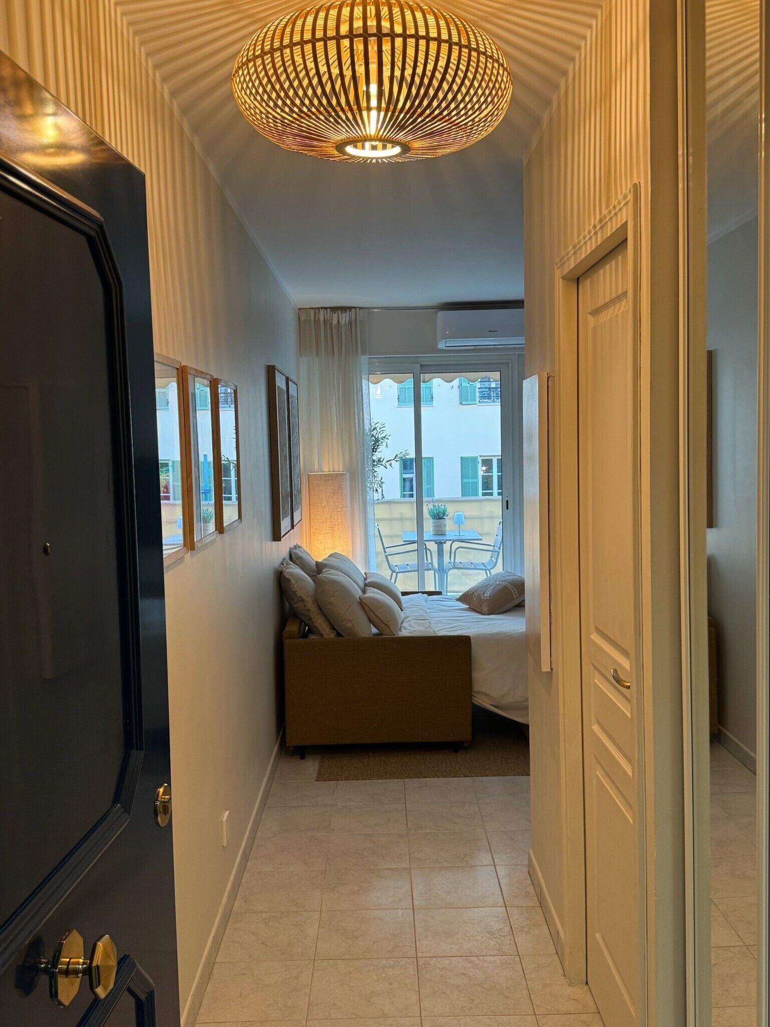 Habitación de hotel con cama, ventana con vistas al exterior, puerta y pasillo.