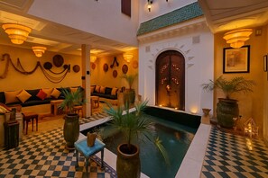 A lobby with a checkered floor, a central pool, sofas, and wall-mounted lighting. - Agafay, Riad Belikoss Pool & SPA (Marrakech)