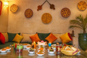 A dining area with a table set for a meal, a sofa with cushions, and decorative wall hangings. - Agafay, Riad Belikoss Pool & SPA (Marrakech)