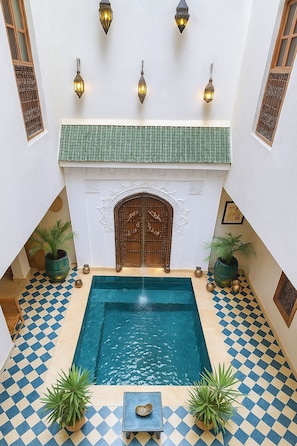 A pool area with a checkered floor, a central pool, decorative wall sconces, and a large wooden door with intricate carvings. - Agafay, Riad Belikoss Pool & SPA (Marrakech)