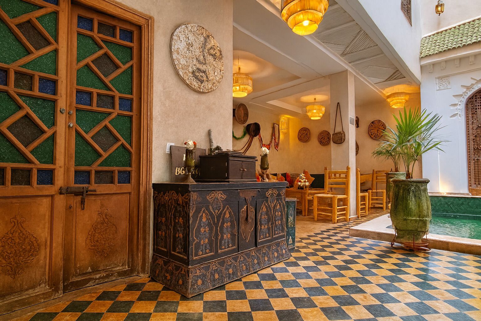 A lobby with a checkered floor, a wooden door with glass panels, a decorative cabinet, and a small pool area.