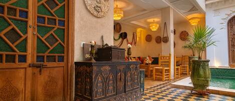 A lobby with a checkered floor, a wooden door with glass panels, a decorative cabinet, and a small pool area.