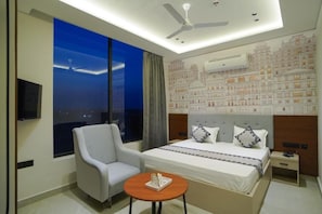 Een hotelkamer met een groot bed, een stoel, een klein tafeltje en uitzicht op de stad.