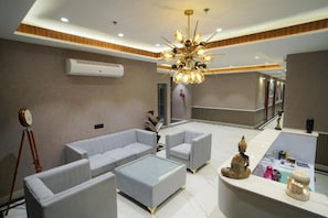 Een moderne lobby met een receptiebalie, een zithoek en een decoratieve plafondlamp.