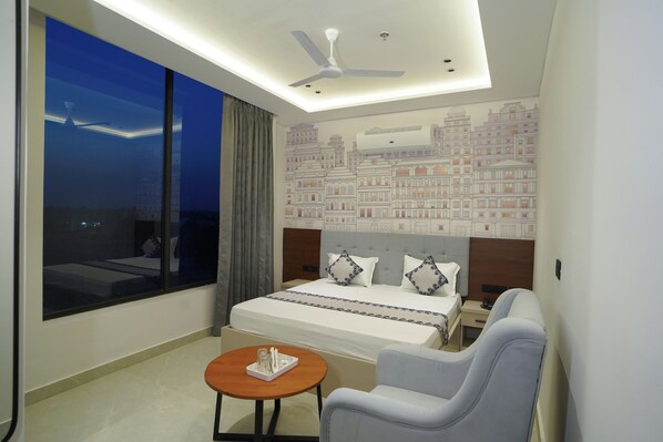 A hotel room with a large bed, a seating area, a small table, and a view of the cityscape.