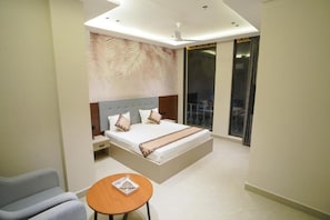 Een moderne slaapkamer met een groot bed, een klein tafeltje en een balkon met gordijnen.