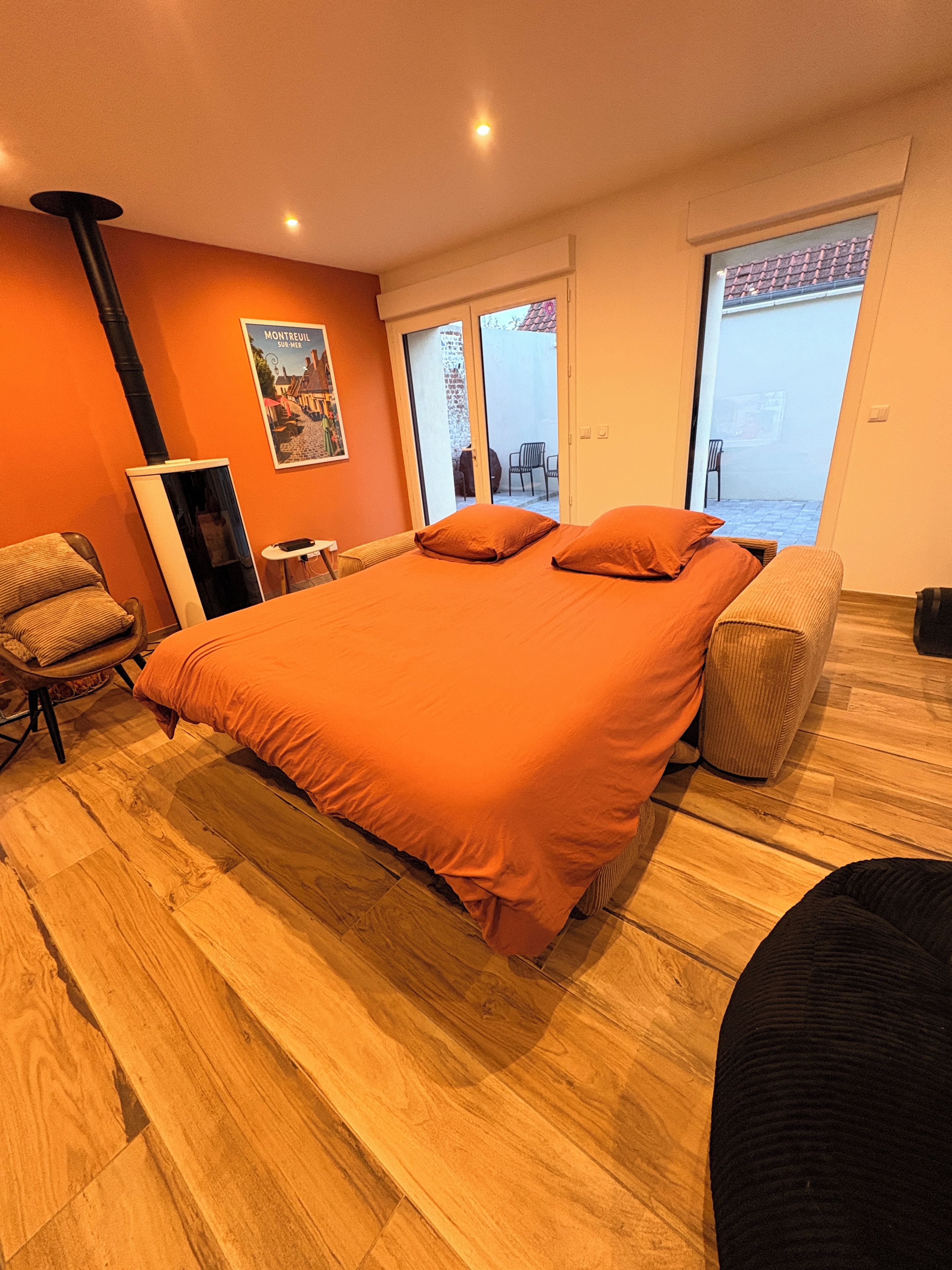 Een slaapkamer met een groot bed, een houten vloer, een stoel, een klein tafeltje en een poster aan de muur.