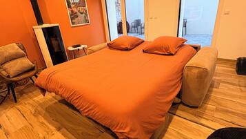 Een slaapkamer met een groot bed, een houten vloer, een stoel, een klein tafeltje en een poster aan de muur.