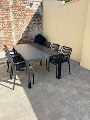 Eine Außenpatio mit einem Metalltisch und Stühlen, einer Ziegelwand und einer beigen Wand.