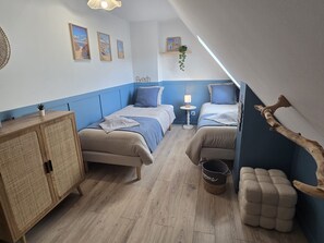 Ein Schlafzimmer mit zwei Betten, einem Holzschrank, einem kleinen Tisch mit Lampe und einer hängenden Pflanze.