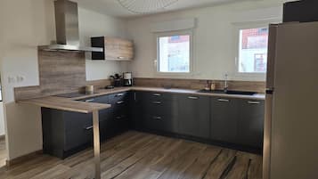 Et moderne køkken med mørke skabe, en træbordplade og et unikt loftslampesæt.