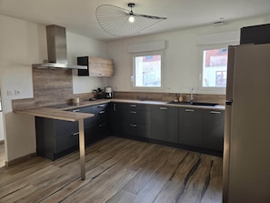 A modern kitchen with dark cabinetry, a wooden countertop, and a unique ceiling light fixture. - Montr'oeil d'Opale (Écuires)