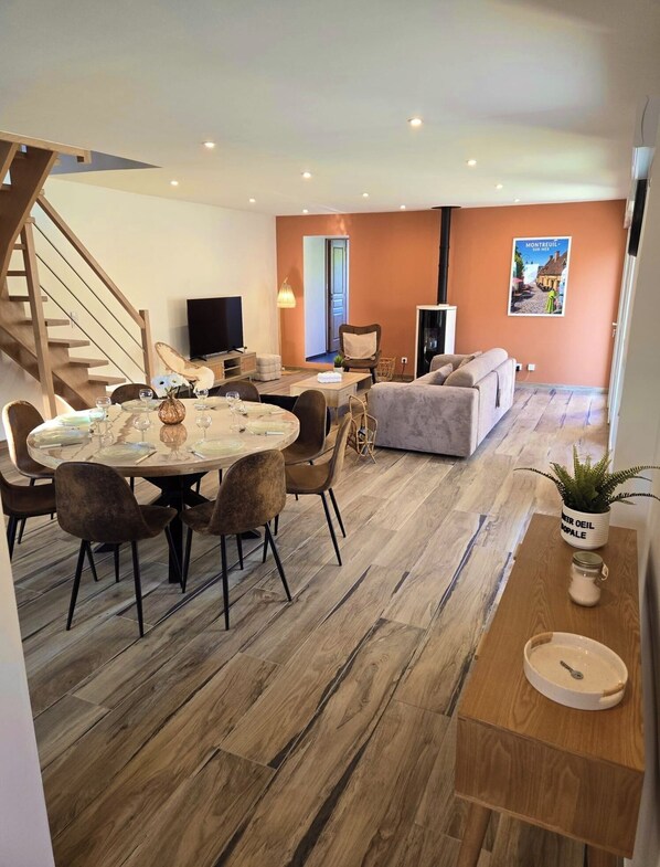 Ein modernes Wohnzimmer mit Essbereich, einer Couch, einem Fernseher und einer Treppe.