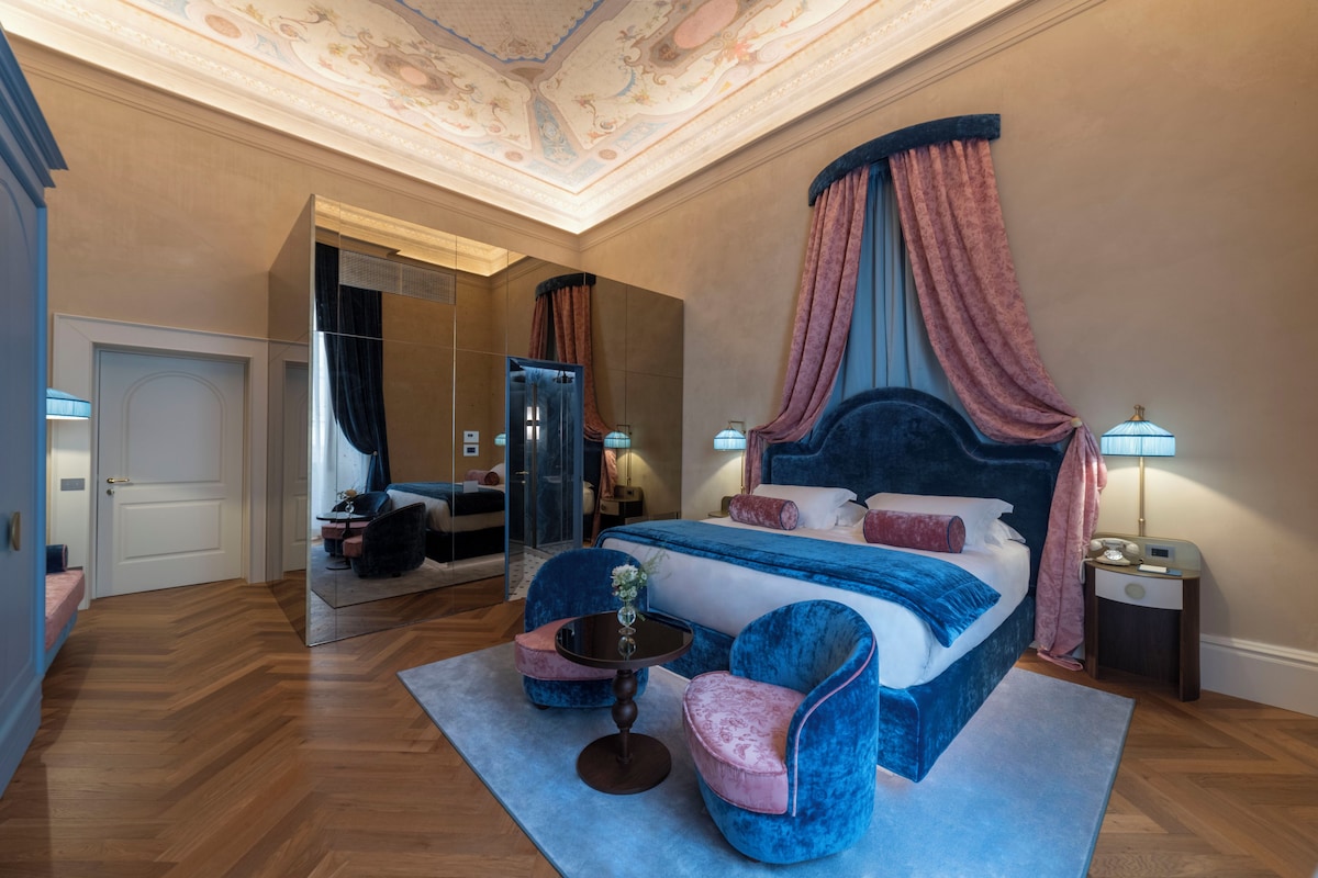 A bedroom with a large bed, a canopy, a mirror, a desk, and a chair.
