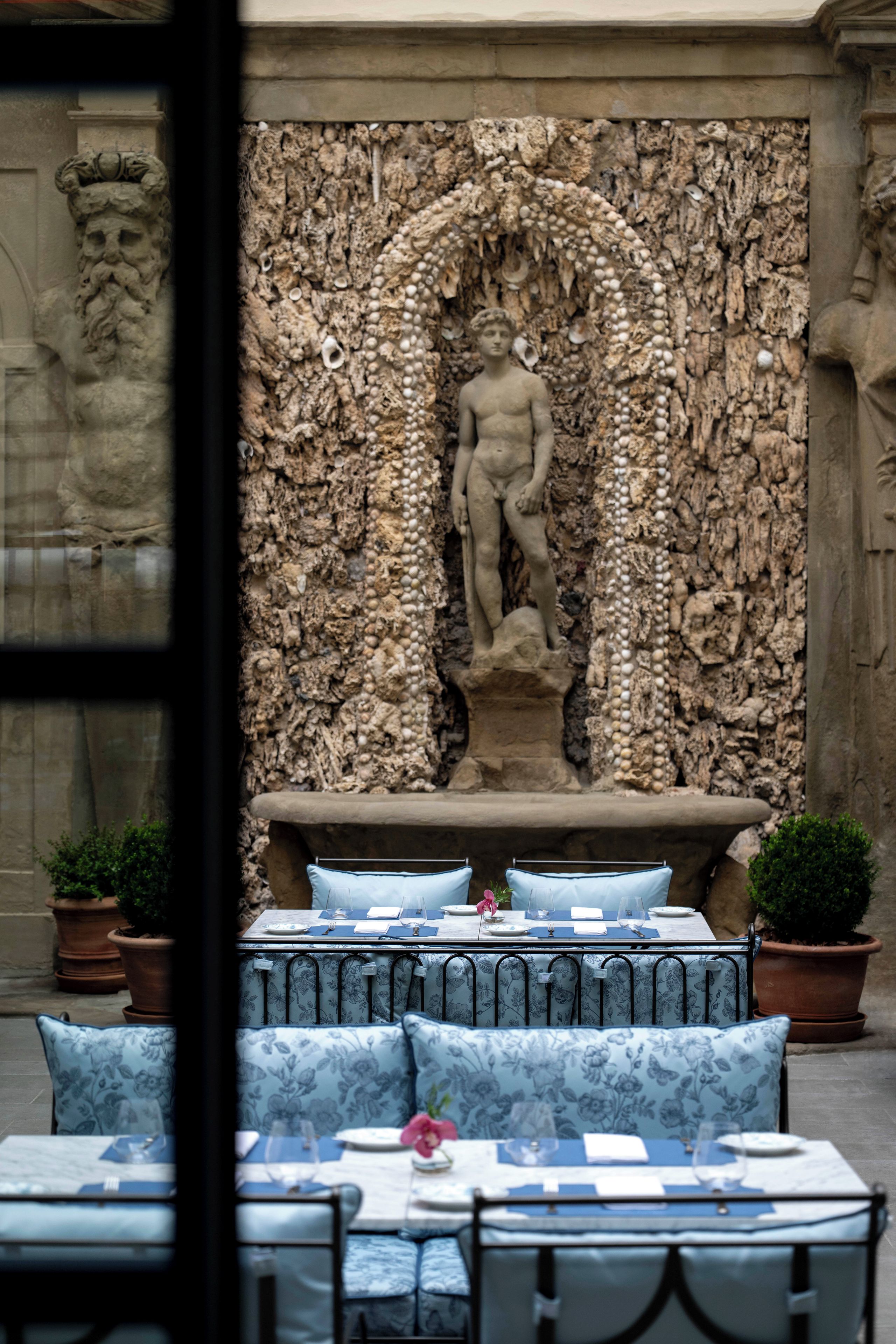 Eine steinerne Statue einer männlichen Figur in einer Nische, umgeben von einer reliefartigen Steinwand mit rauer, natürlicher Struktur.