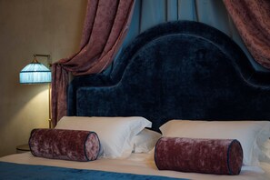 Una cama con cabecera oscura, almohadas blancas y colcha azul.