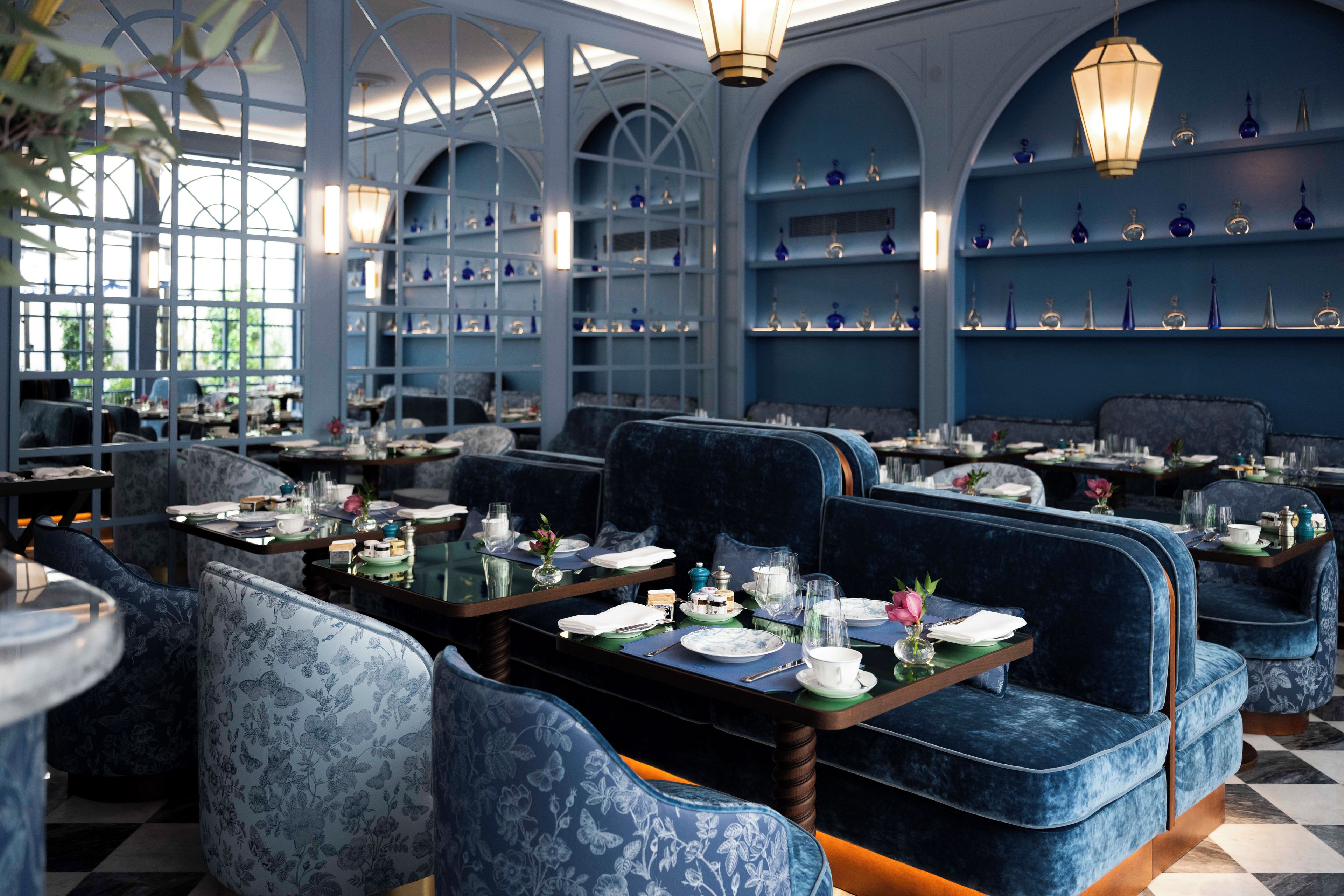 Un restaurant avec des banquettes bleues, des tables dressées avec des assiettes, des verres et des couverts, et un plafond décoratif agrémenté de luminaires suspendus.