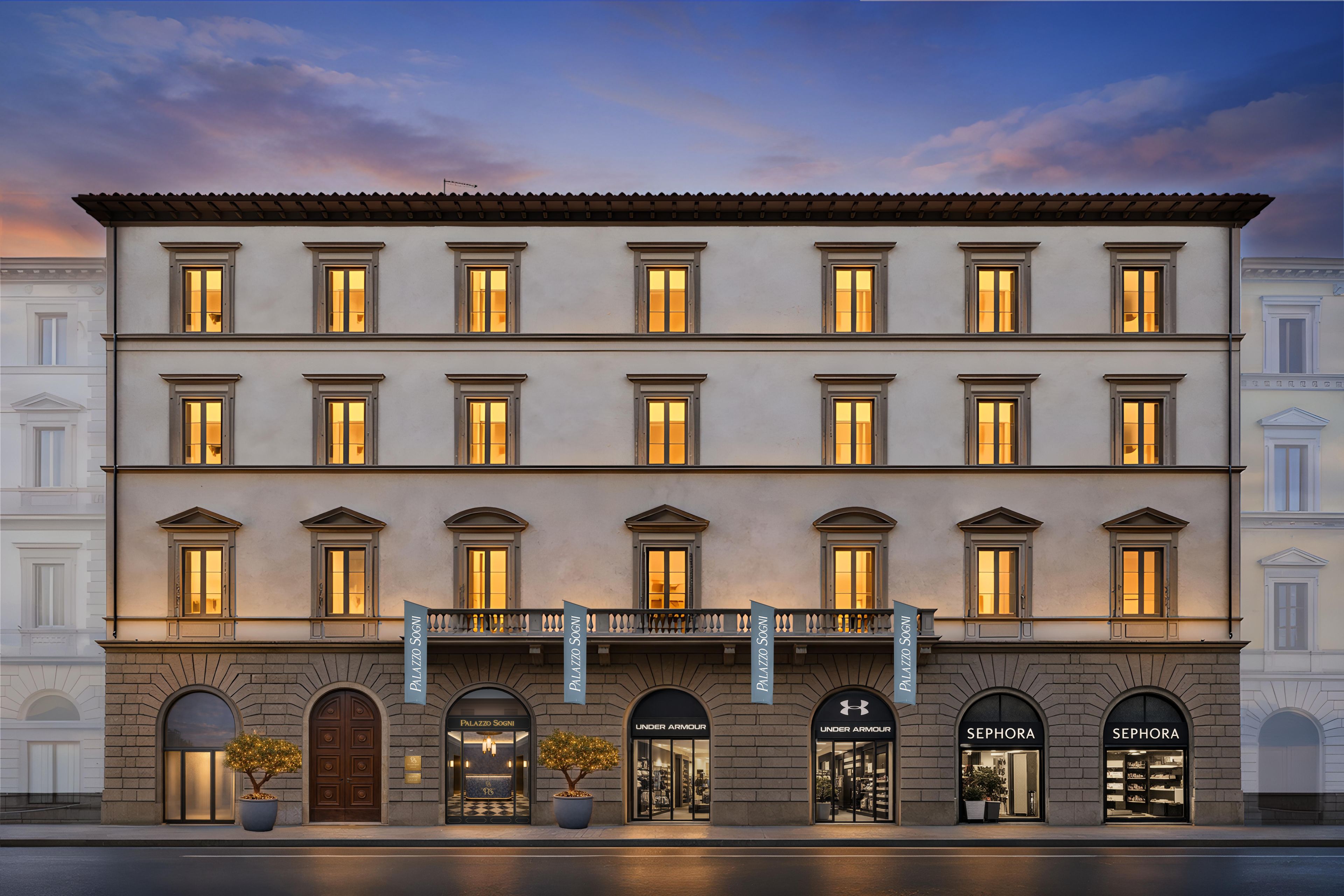 Un edificio de varios pisos con una fila de tiendas en la planta baja, incluyendo marcas como Under Armour y Sephora.