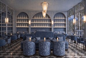 A restaurant interior with checkered flooring, blue upholstered seating, and a wall of crystal decanters. - Palazzo Sogni (Firenze)
