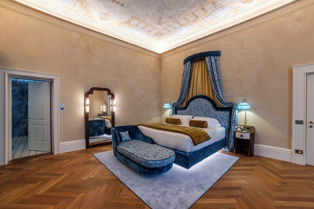 A bedroom with a four-poster bed, a nightstand, a mirror, and a wooden floor.