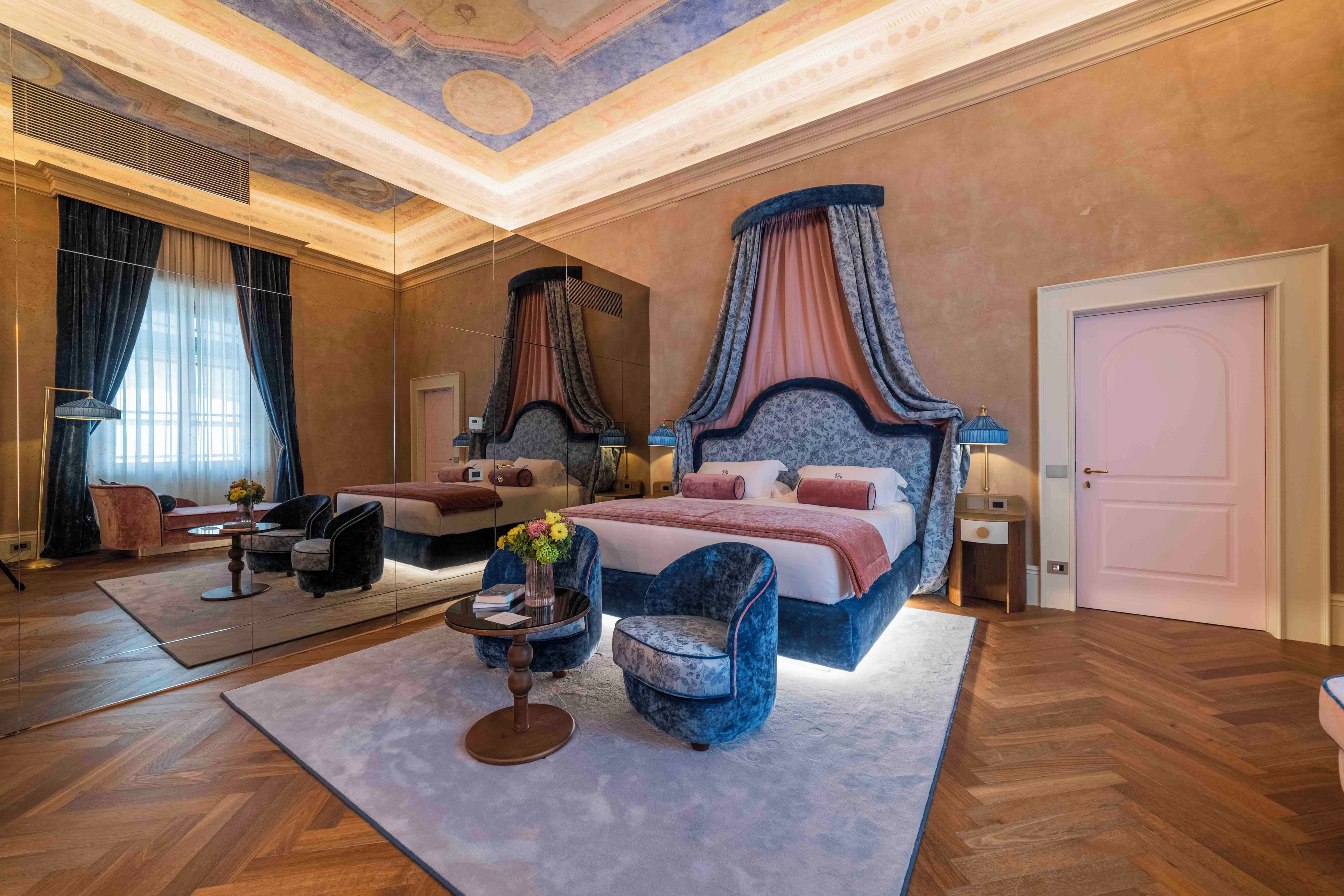 Ein geräumiges Schlafzimmer mit einem großen Bett, einem kleineren Bett, einer Sitzecke mit Tisch und Stühlen sowie einem großen Spiegel.