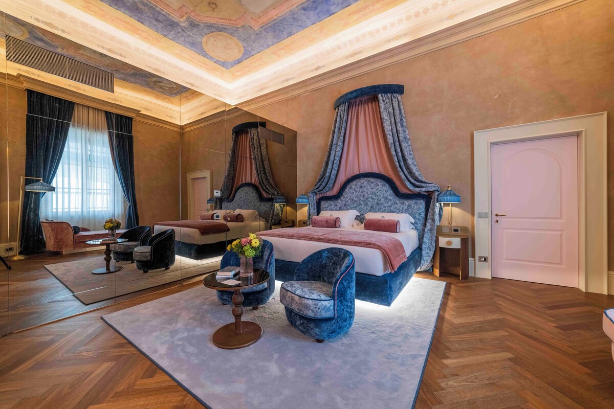 A spacious bedroom with a large bed, a smaller bed, a sitting area with a table and chairs, and a large mirror.