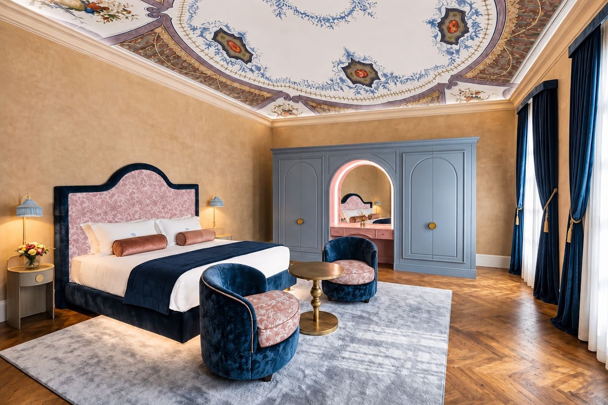 A bedroom with a bed, two armchairs, a desk, and a wardrobe.