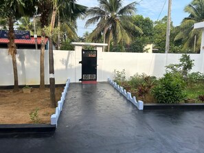 Une entrée fermée par un portail, avec un chemin en béton menant à un bâtiment.