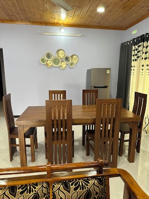 A dining area with a wooden table and chairs, a decorative wall piece, and a refrigerator. - Large, Peaceful 5‑Bedroom Home Just Steps from Jaffna Town (Jaffna)