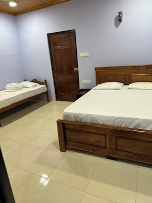 A bedroom with a large bed, a smaller bed, a wooden door, and a tiled floor.