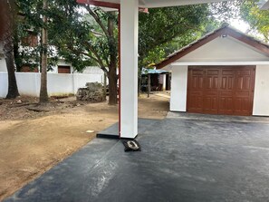 A covered outdoor area with a concrete floor, a white pillar, and a brown garage door.