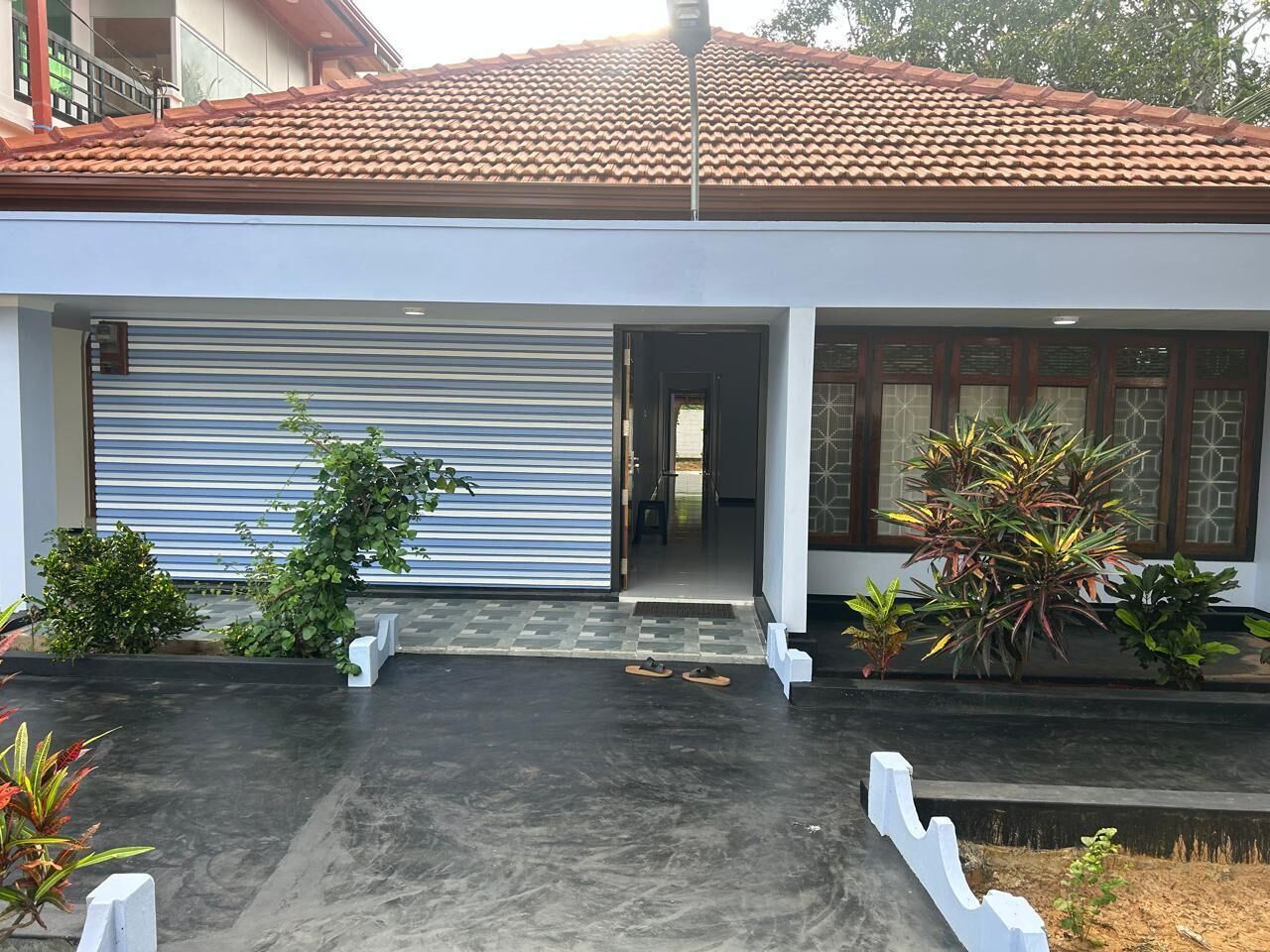 A residential building with a closed garage door, a concrete driveway, and potted plants.