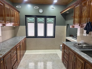 A kitchen with wooden cabinets, a window with blinds, a sink, and a stove. - Large, Peaceful 5‑Bedroom Home Just Steps from Jaffna Town (Jaffna)