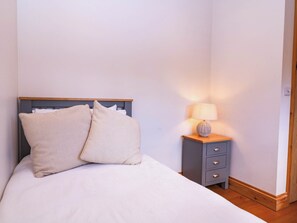 Ein Bett mit zwei Kissen, ein Nachttisch mit einer Lampe und ein Holzboden.