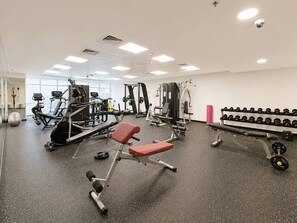 Ein Fitnessstudio mit unterschiedlichen Trainingsgeräten, darunter Bänke, Kurzhanteln und Kraftgeräte.